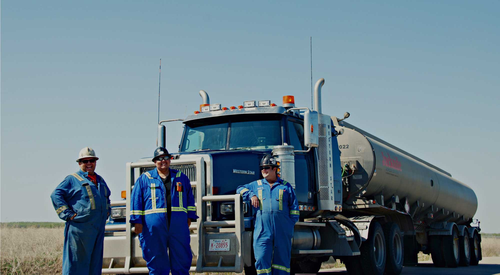 3 men with blue coveralls in front of semi truck